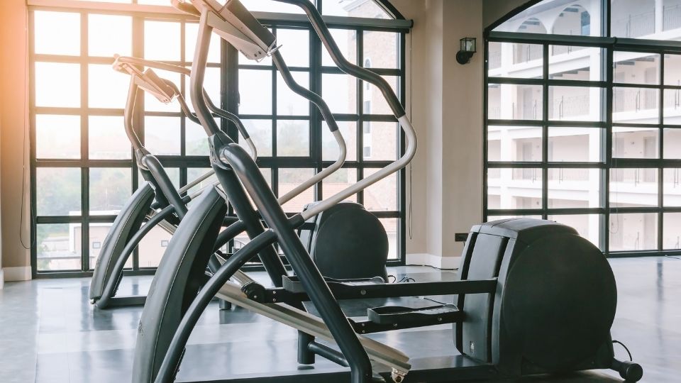 Moderné fitness stroje v svetlej telocvični s veľkými oknami.