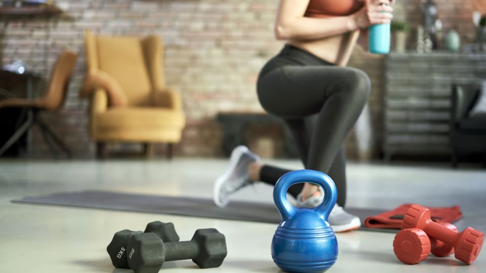 Žena cvičí s činkami a kettlebellom v domácom prostredí.