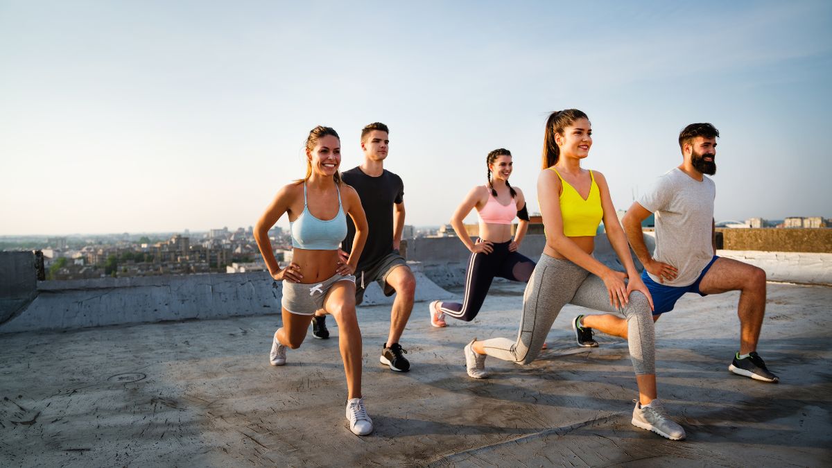 HIIT: Spáľte maximum kalórií v minimálnom čase. Skupina mladých ľudí cvičí na streche budovy, vykonávajú výpady.